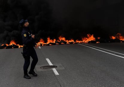 Un policía enfrente de una barricada ardiendo en Gijón.