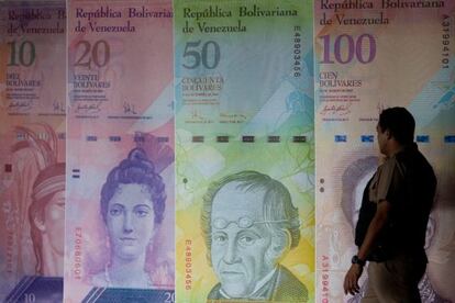 Un hombre camina frente a unos afiches de billetes venezolanos.