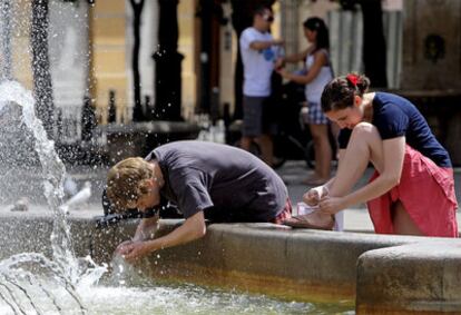 Un joven se refresca este mediodía en la fuente situada en la céntrica plaza de la Virgen de Valencia.
