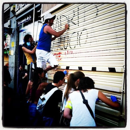 Un grupo de acampados en Sol limpian las pintadas de un comercio.