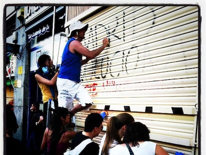 Un grupo de acampados en Sol limpian las pintadas de un comercio.