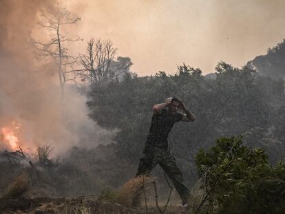 Un hombre se cubría del agua lanzada desde un helicóptero que combate un incendio en Rodas, Grecia.