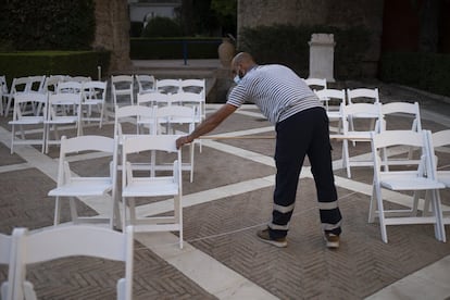 Un operario distribuye las sillas de dos en dos en el Real Alcázar de Sevilla, para lo que utiliza una cuerda que hace de tiralíneas y un vara de madera de 1,5 metros de longitud para tomar la distancia.