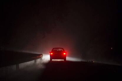 Un coche circula a través del humo de un incendio cercano, en Entrimo (Galicia).