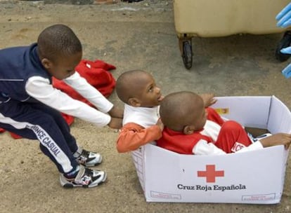 Tres de los niños rescatados de una patera en el Estrecho juegan con una caja de Cruz Roja.