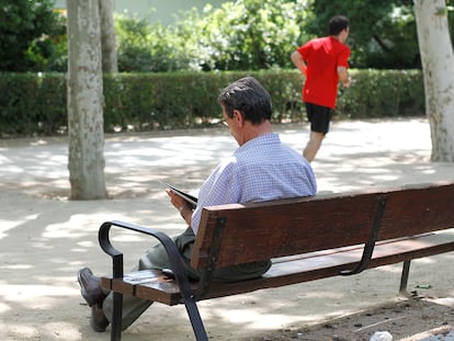 Un hombre lee, a la sombra, en un banco de El Retiro.