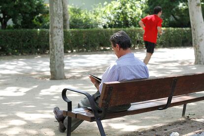 Un hombre lee un libro en un banco del Parque del Retiro en Madrid.