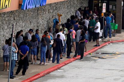 Vista de una cola formada a la entrada de una tienda donde la gente espera para compra provisiones.