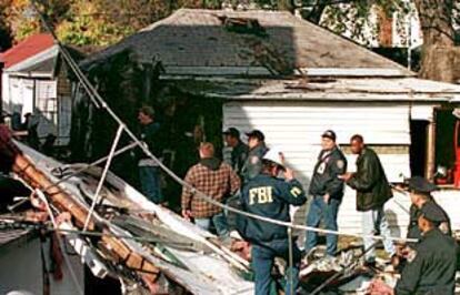 Policías de Nueva York y miembros del FBI investigan entre los restos del fuselaje del avión caídos sobre una casa de Rockaway, en Queens.