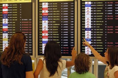 Varios pasajeros consultan un panel de información en Barajas.