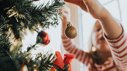 Una niña decora un árbol de Navidad.