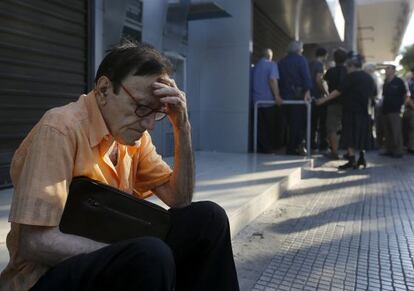 Un pensionista descansa a les portes d'un banc tancat, davant el qual s'han concentrat nombrosos usuaris des de primera hora.