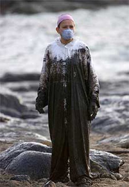 Una voluntaria manchada del fuel que trata de retirar en la playa de Muxía, en la Costa da Morte.