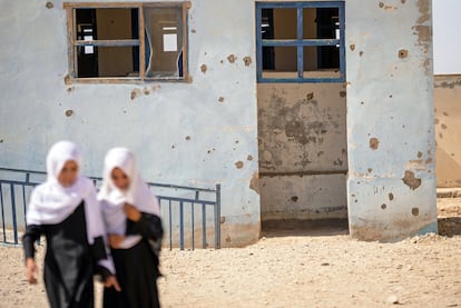 Dos adolescentes caminan junto a una escuela que tiene agujeros en la fachada por disparos en Afganistán. Cientos de escuelas resultaron dañadas o fueron destruidas durante los años de conflicto en el país, privando a decenas de miles de niños de la posibilidad de acceder a una educación.