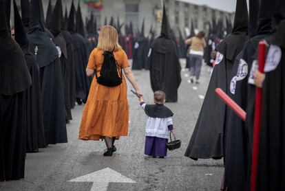 Una mujer lleva de la mano a un niño vestido de monaguillo de la Hermandad de San Bernardo durante la salida procesional de esta cofradía por las calles de Sevilla, el 17 de abril de 2019.