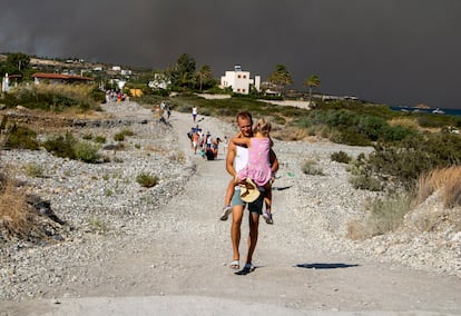 A man carries a child as they leave an area where a forest fire burns, on the island of Rhodes, Greece, Saturday, July 22, 2023