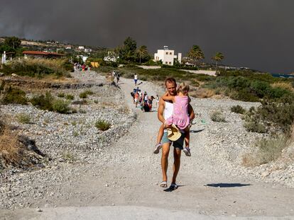 A man carries a child as they leave an area where a forest fire burns, on the island of Rhodes, Greece, Saturday, July 22, 2023