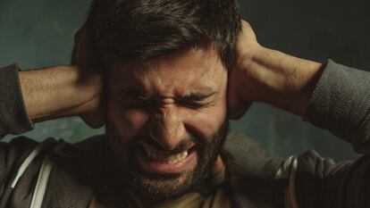 Close up portrait of young man in pain closing eyes and plugging ears with his hands protecting from loud noise