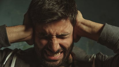 Close up portrait of young man in pain closing eyes and plugging ears with his hands protecting from loud noise