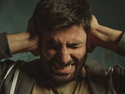 Close up portrait of young man in pain closing eyes and plugging ears with his hands protecting from loud noise