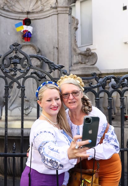 Dos mujeres se fotografían este miércoles delante de la estatua del Manneken Pis en Bruselas (Bélgica), vestida con el traje tradicional ucranio para conmemorar el día nacional.