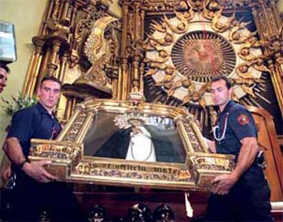 Dos bomberos sostienen el lienzo con la imagen de la Virgen de la Paloma en la iglesia del mismo nombre.