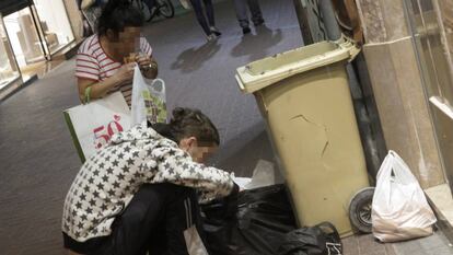 Dos personas buscando comida en unos contenedores de basura.