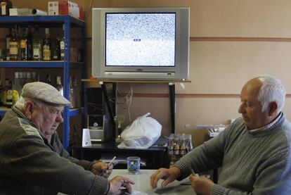 Dos vecinos juegan una partida de cartas ante la televisin sin se?al de un bar de Valdaracete.