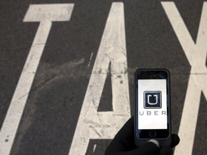 El logo de Uber en un smartphone junto a un r&oacute;tulo de taxi.