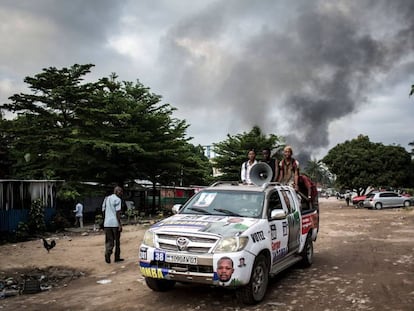 Un automóvil con propaganda electoral cerca de un incendio en un almacén de máquinas para votar, este jueves en Kinshasa.