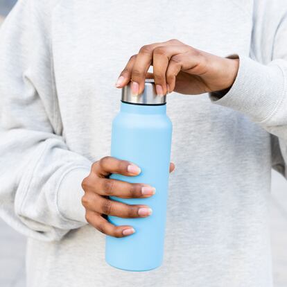 An unrecognizable black woman opening a bottle of water with her hands in the street after doing outdoor sports