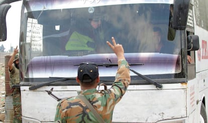 Soldados sírios fazem o símbolo da vitória em frente a um ônibus que evacua rebeldes em Duma, nos arredores de Damasco.