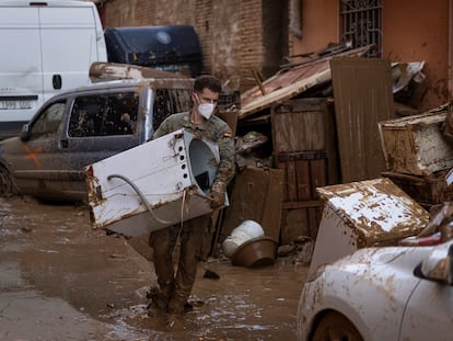 Un miembro del Ejército tira a la calle una lavadora del interior de una vivienda de Catarroja que el agua inutilizó.