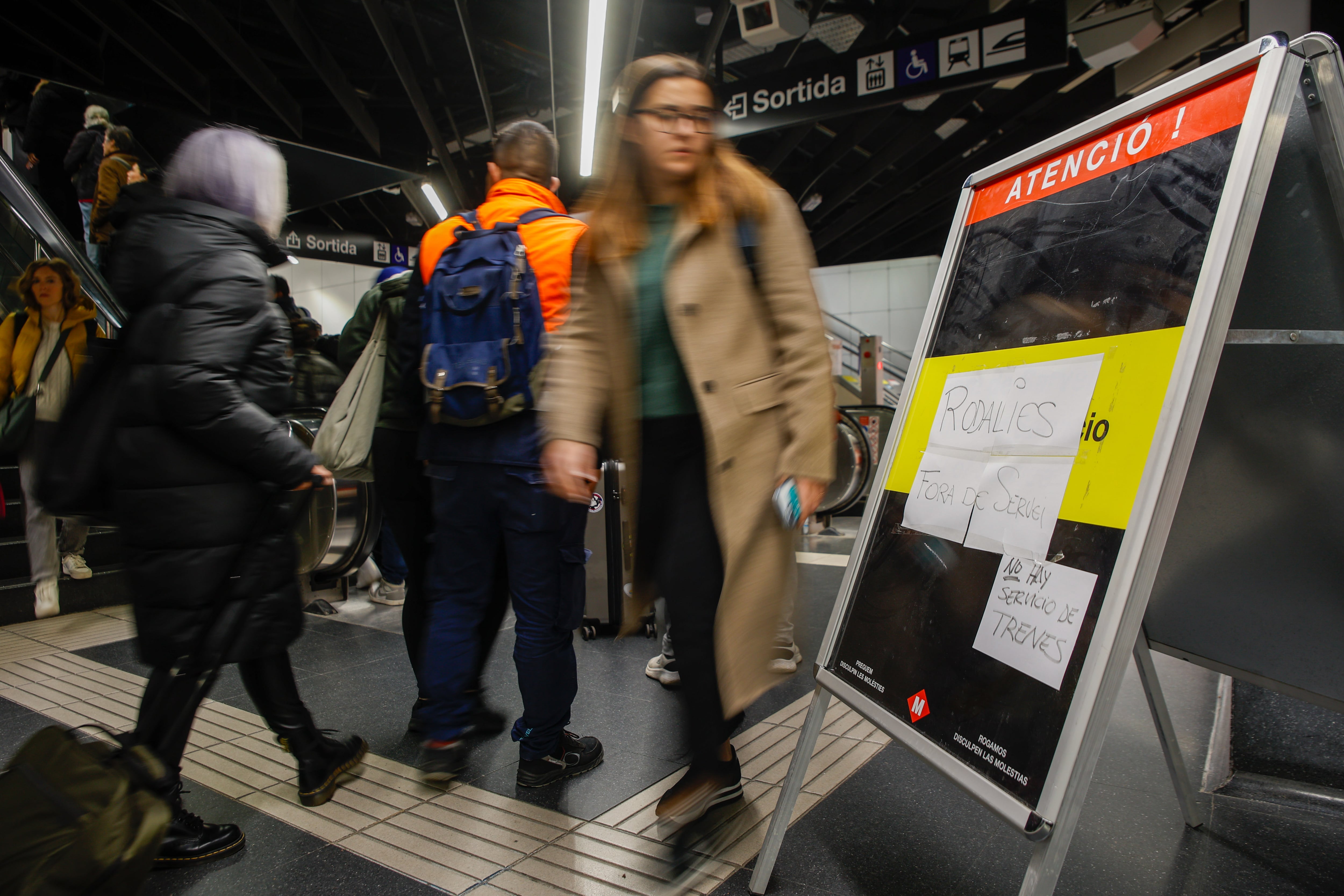 Varias personas pasan por delante de un cartel que informa de la suspensión del servicio de Rodalies en toda Cataluña, este miércoles, en la estación de Sants (Barcelona).