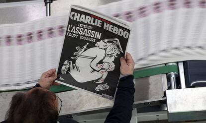 Un empleado de una imprenta sostiene del semanario francés Charlie Hebdo con el título 'Un año después, el asesino sigue en la carrera', en enero de 2016.