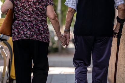 Un hombre y una mujer mayores caminando cogidos de la mano por el barrio de Puerta del Ángel, Madrid.