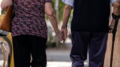 Un hombre y una mujer mayores caminando cogidos de la mano por el barrio de Puerta del Ángel, Madrid.