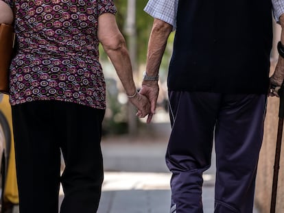 Un hombre y una mujer mayores caminando cogidos de la mano por el barrio de Puerta del Ángel, Madrid.