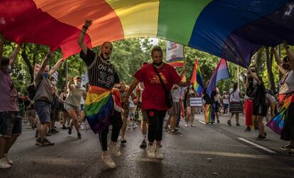 Dos jóvenes pasan debajo de una bandera multicolor durante la manifestación del Orgullo en Madrid, el 3 de julio de 2021.