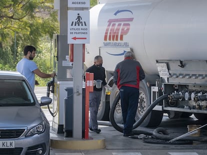 Dos operarios llenan un depósito de carburante de una estación de servicio en Sevilla mientras un cliente reposta.