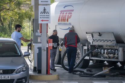 Dos operarios llenan un depósito de carburante de una estación de servicio en Sevilla mientras un cliente reposta.