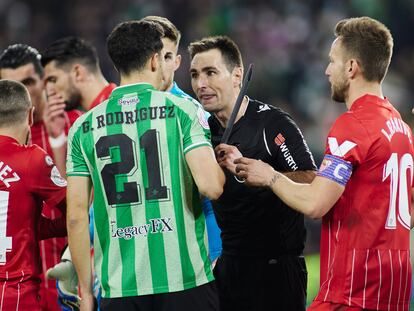 El árbitro De Burgos Bengoechea muestra el palo que impactó a Jordán al bético Guido Rodríguez.