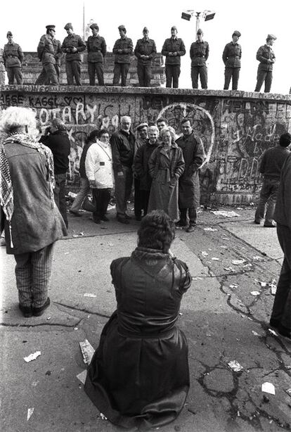 Un grupo de personas se fotografía a los pies del Muro y de un grupo de vopos que intentan evitar los saltos de las primeras horas.