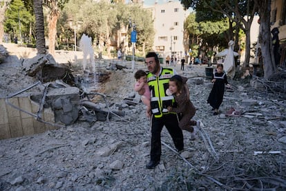 Un rescatista evacúa a dos niños del lugar donde impactó un misil lanzado desde Irán en Haifa (Israel).