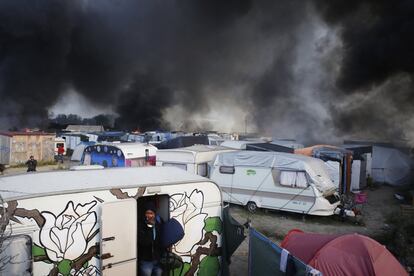 Un hombre sale de una caravana con sus pertenencias mientras el humo cubre las tiendas del campo de migrantes conocido como 'la Jungla' de Calais (Francia), el 26 de octubre de 2016.