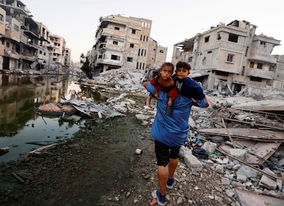 Un hombre camina con sus hijos entre los escombros de edificios destruidos por los bombardeos israelíes en Jan Yunis (Gaza), el domingo.