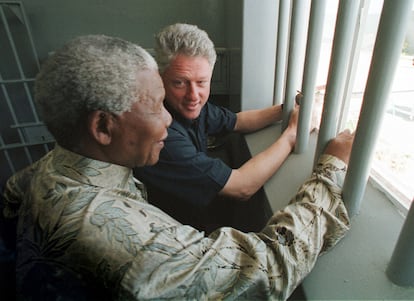 Mandela mira a través de los barrotes (1998) de la celda número 5, el lugar donde estuvo encarcelado durante 18 años, en Robben Island. Le acompaña el entonces presidente de Estados Unidos, Bill Clinton.