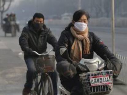Una mujer china (dcha) se desplaza en bicicleta eléctrica y un hombre (izq) en bicicleta normal por Pekín.