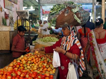 Una mujer carga con hojas de col mientras compra en un puesto de fruta de un mercado de Ahmedabad, India.