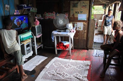 Interior de uma casa quilombola, com chão de madeira. Algumas famílias têm televisão e rádio, mas os eletrodomésticos, de modo geral, são escassos. Dois irmãos, Dhemerson (15) e Deiviti (9), assistem desenhos animados na hora do almoço, acompanhados pela vizinha Sabrina (10).